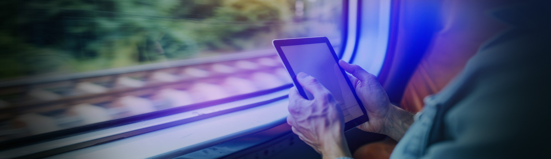 Person using tablet on train with motion-blurred railway tracks outside window