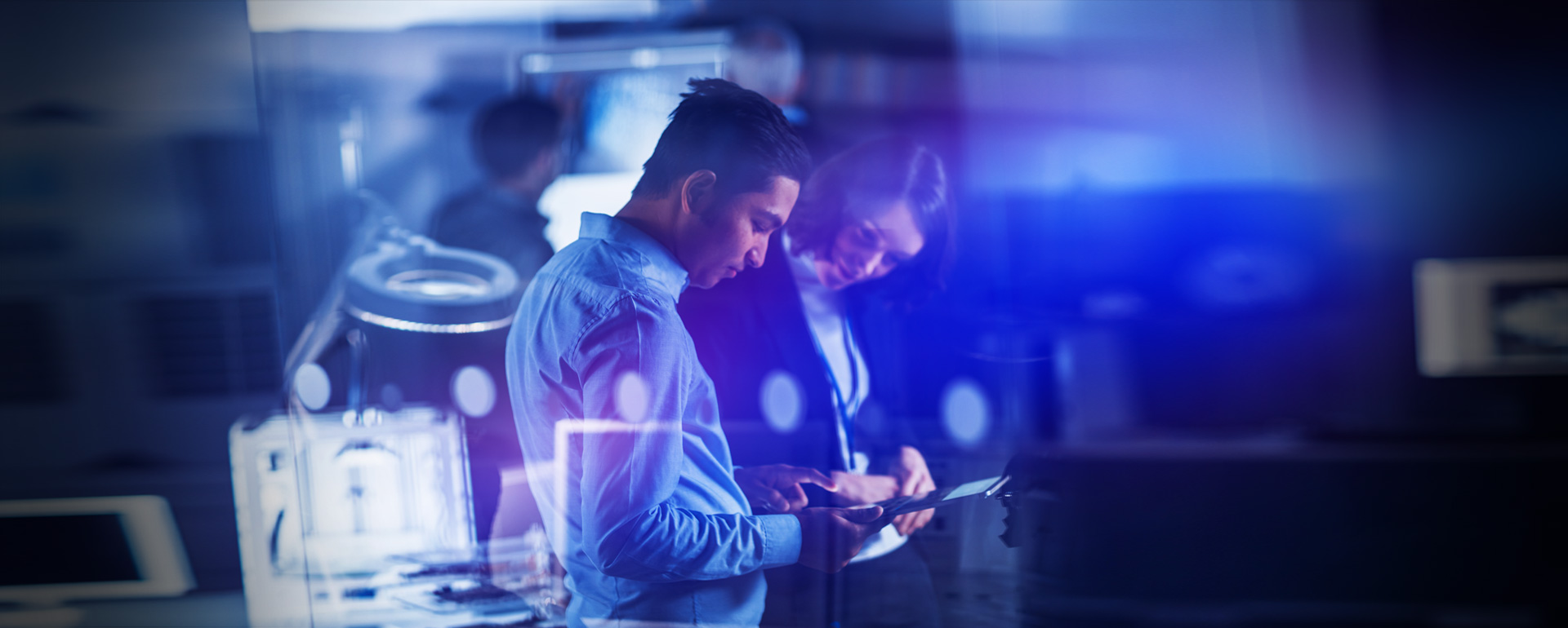 Two professionals reviewing tablet data in modern office with blue lighting overlay