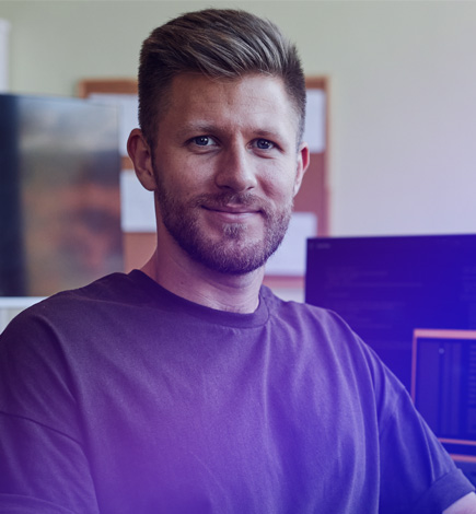 Close-up of person who can provide demo sitting at desk in office with computer screens in background