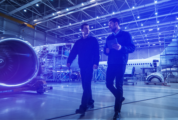 Two professionals walking and talking in aircraft hangar beside jet engine