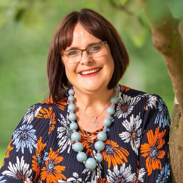 Professional outdoor headshot of person wearing glasses and patterned top with beaded necklace